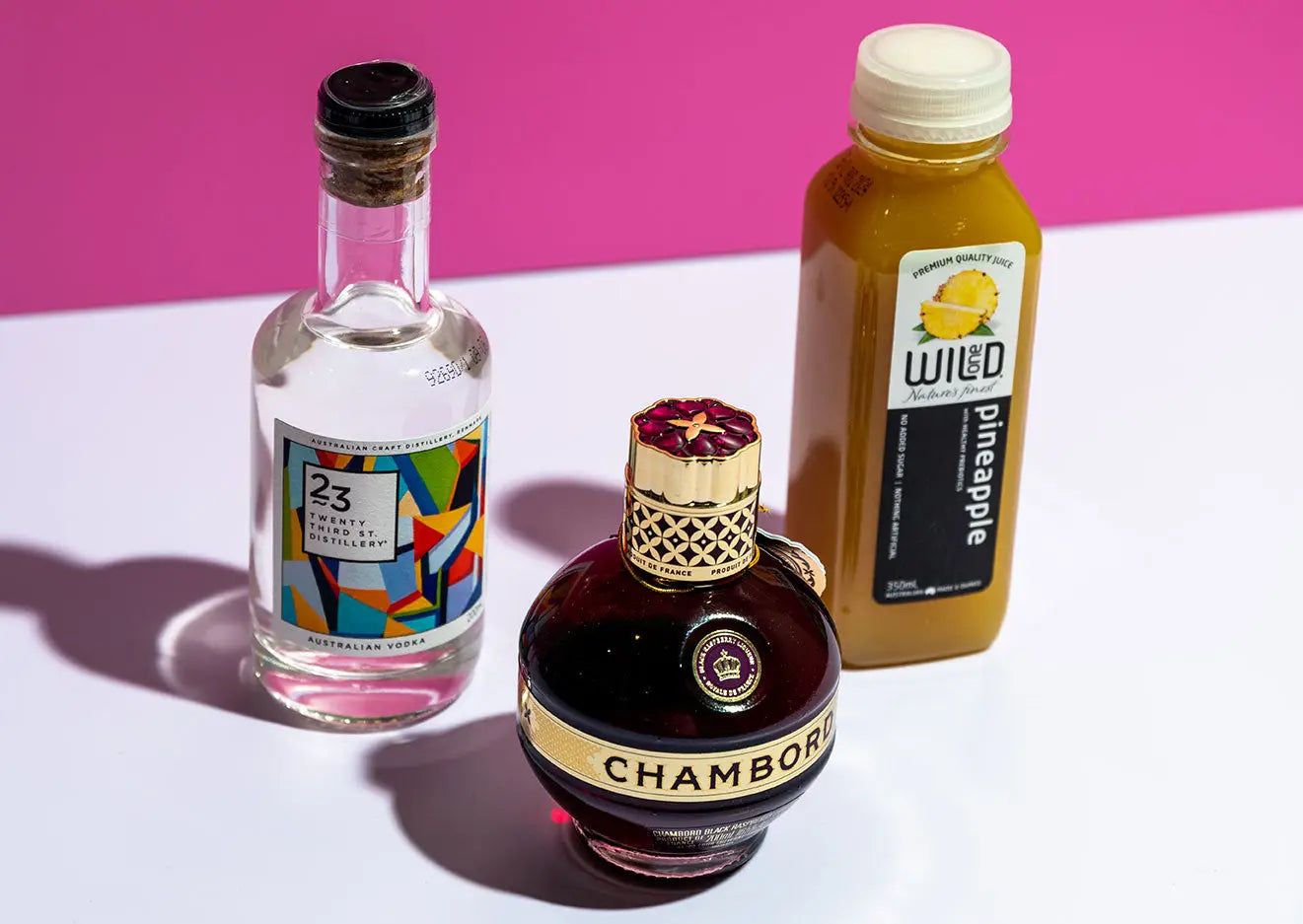 Vodka, juice and Chambord Liqueur on a white table with pink background